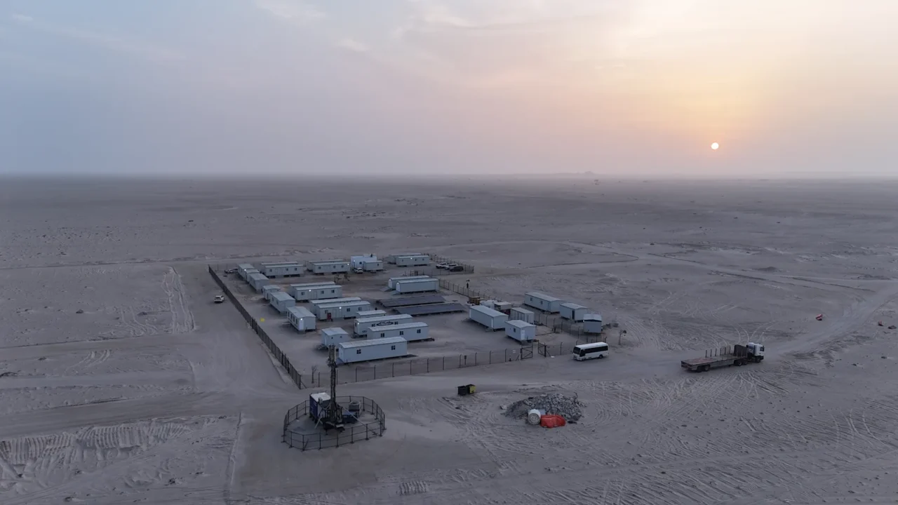 Aerial view of the Etlaq Genesis compound with modular cabins behind a fence in the Duqm desert