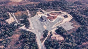 Painting-style aerial view of a cleared launch site with roads and low buildings surrounded by tropical forest near the coast in French Guiana