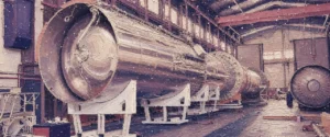 Painting-style illustration: the full Maia rocket lying on white cradles in a long factory hall